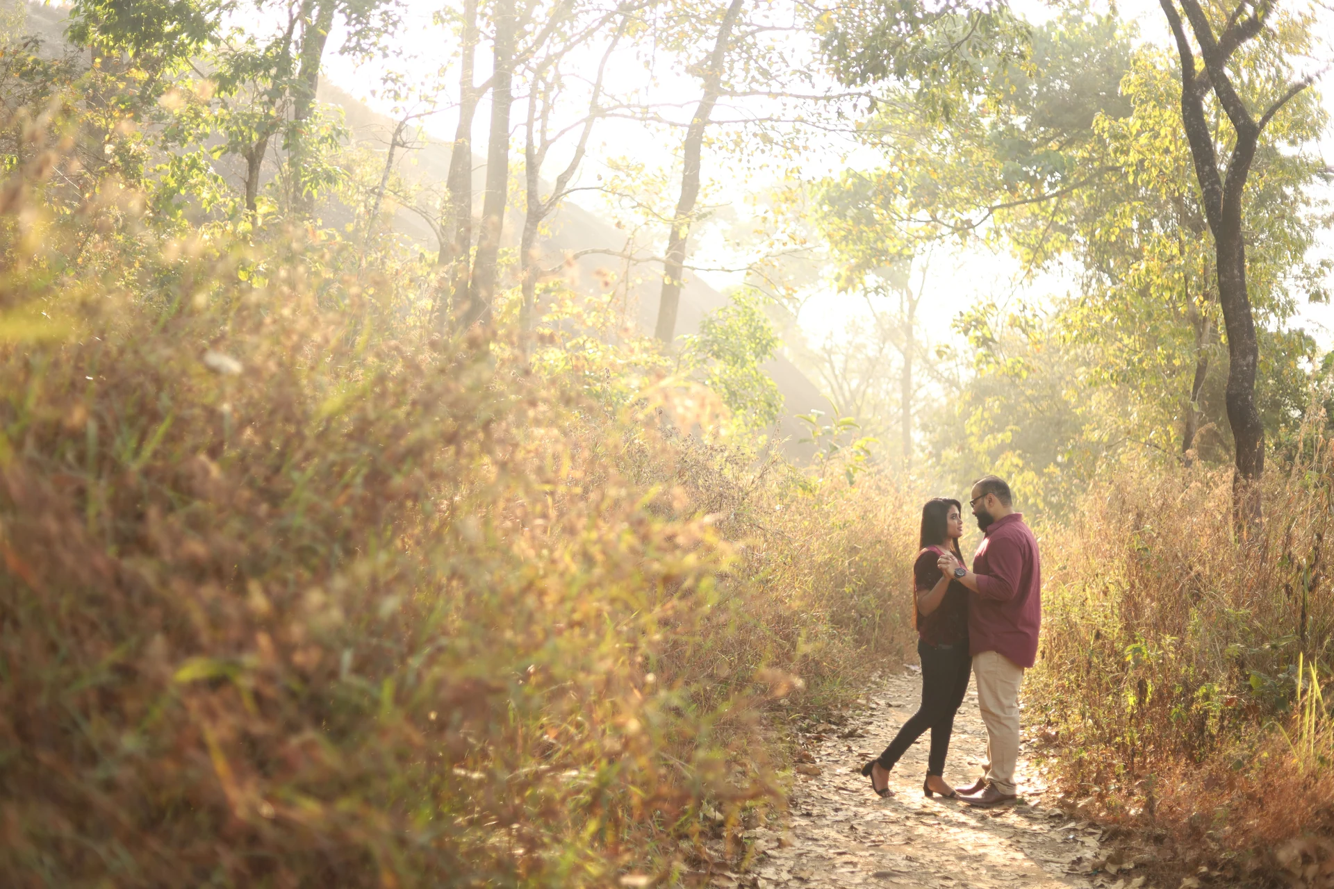 Couple standing together on a sunlit path beneath trees